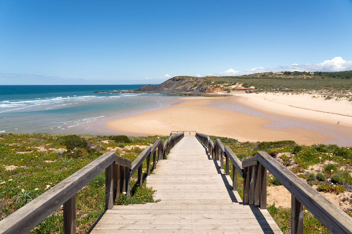 A wooden platform leads down to an expansive sandy beach