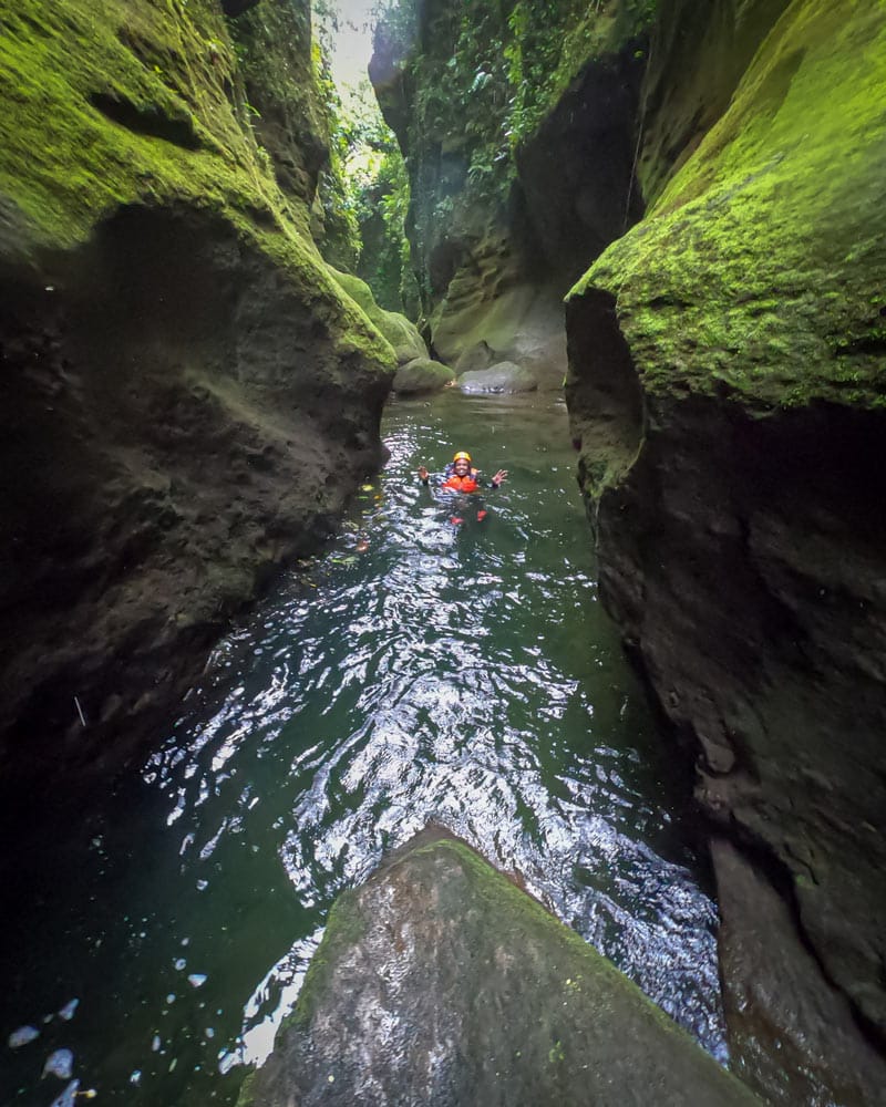 A pool of water with a person in at the bottom of a Canyon in Dominica