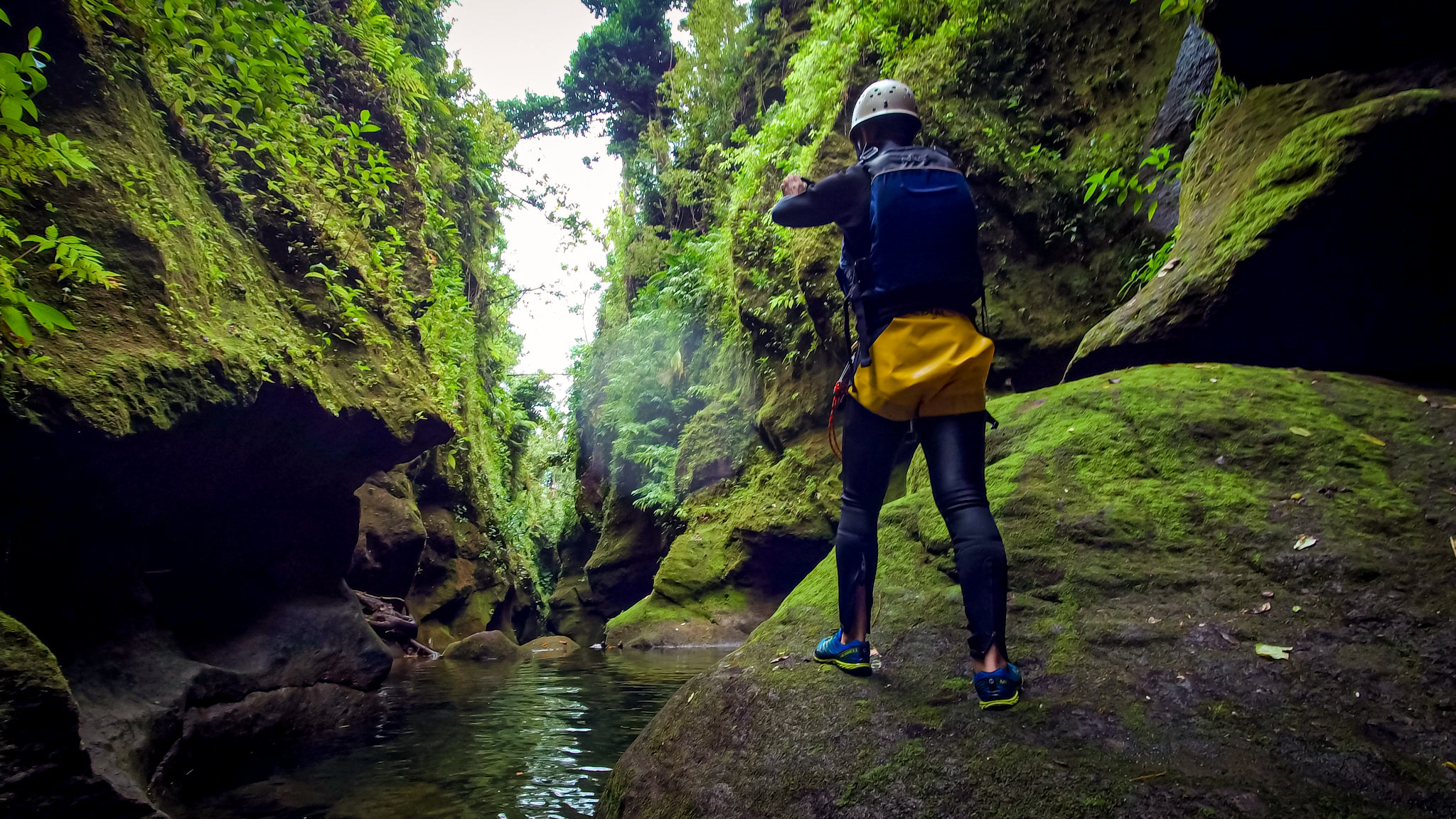 A man stands in a green moss covered canyon taking a photo in Dominica