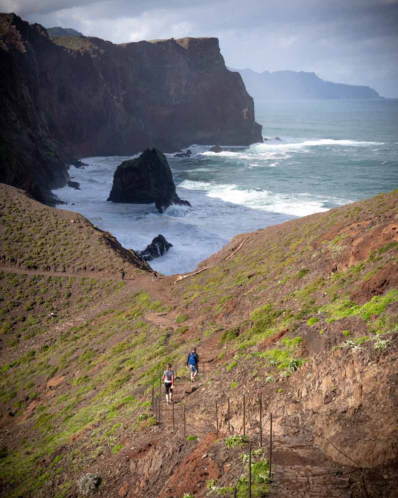 A couple climb the The trail out to Ponta de São Lourenço, with large swell against the cliffs below
