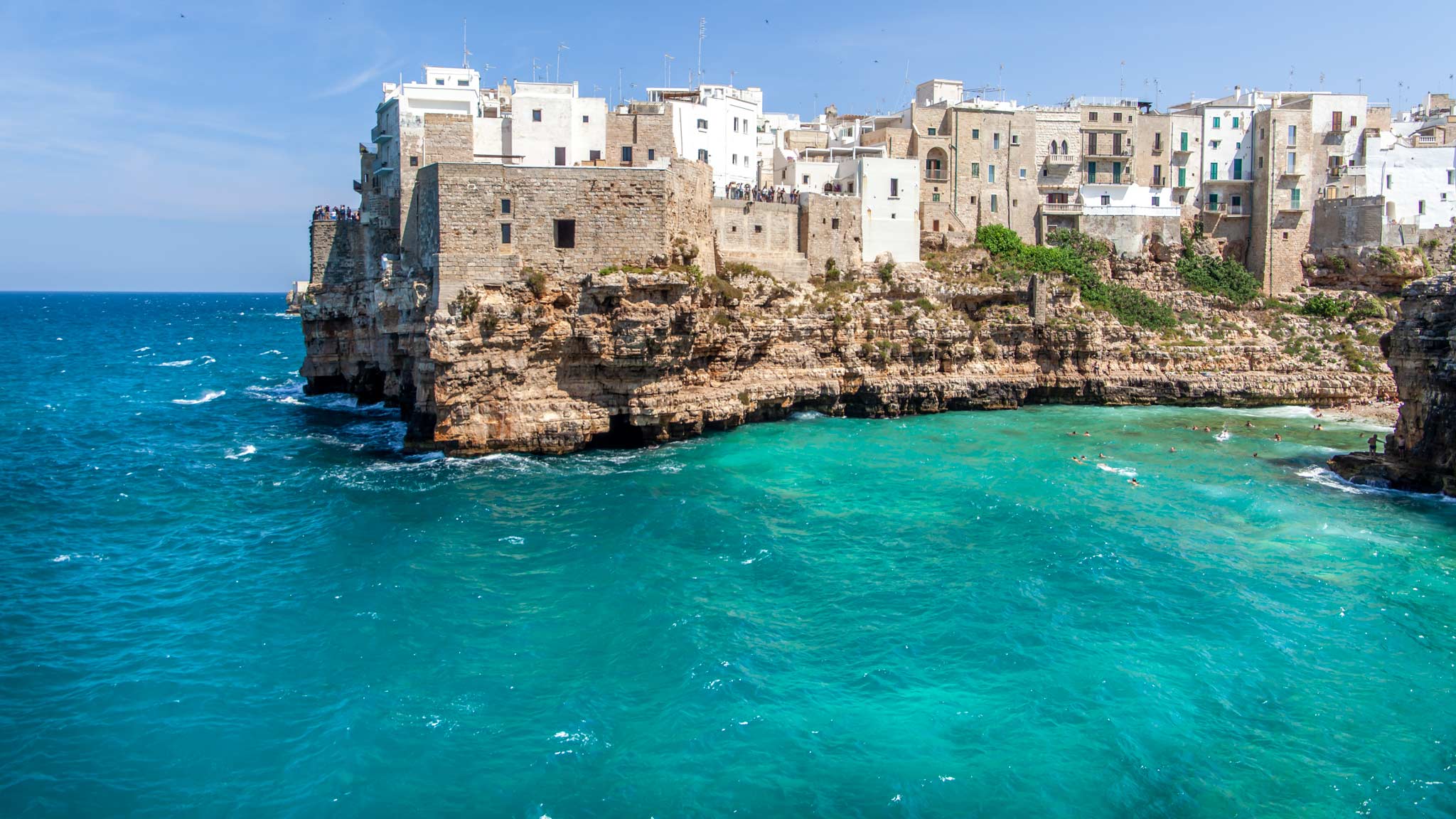 The white-washed cliff buildings stick out over the blue ocean of Polignano a Mare