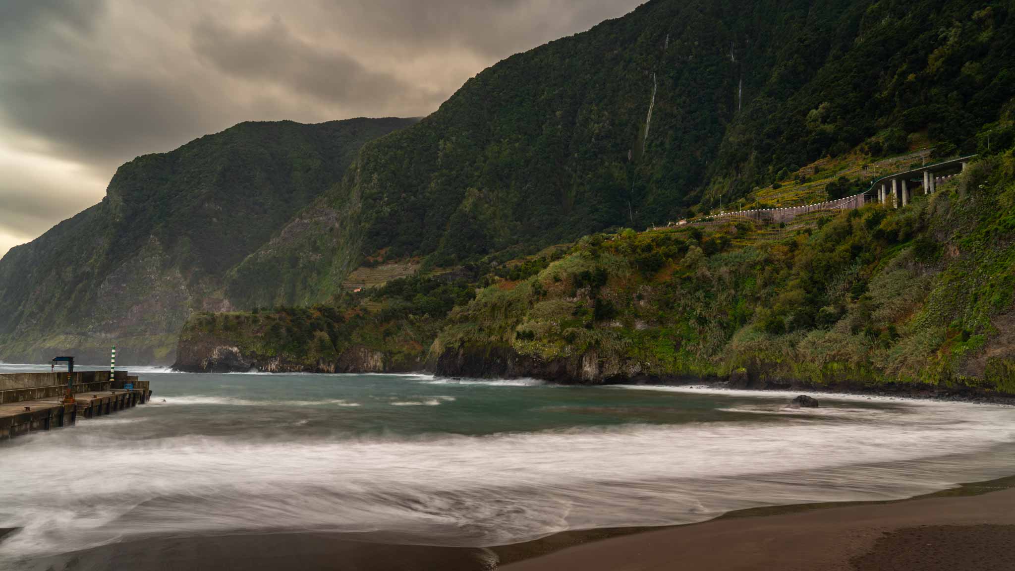 The black sand beach of Seixal with green cliffs and waterfalls