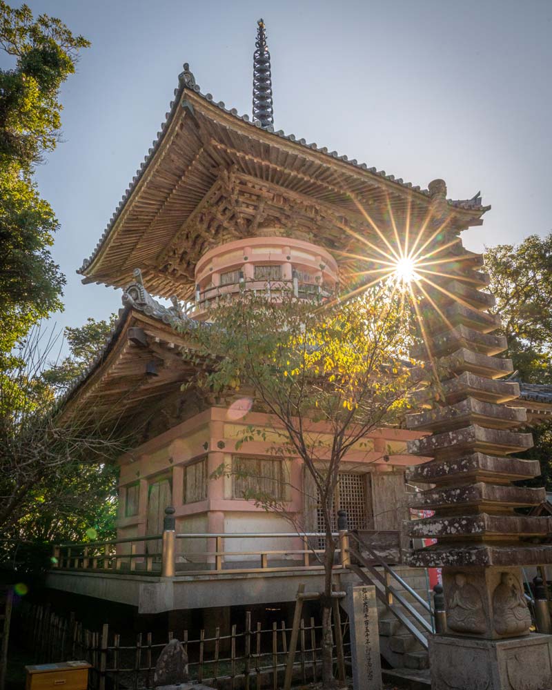 The sun shines behind a pink and white temple on the Shikou temple pilgrimage