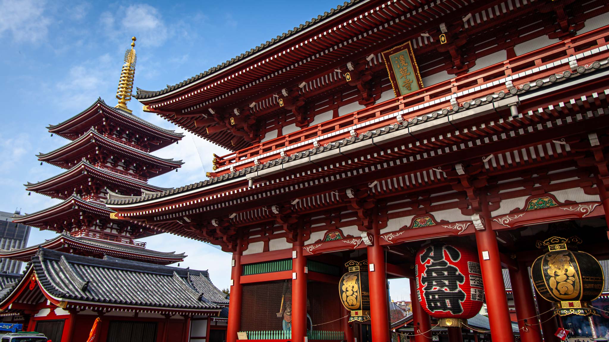 A beautiful red pagoda sits next to a large red temple in the city of Tokyo